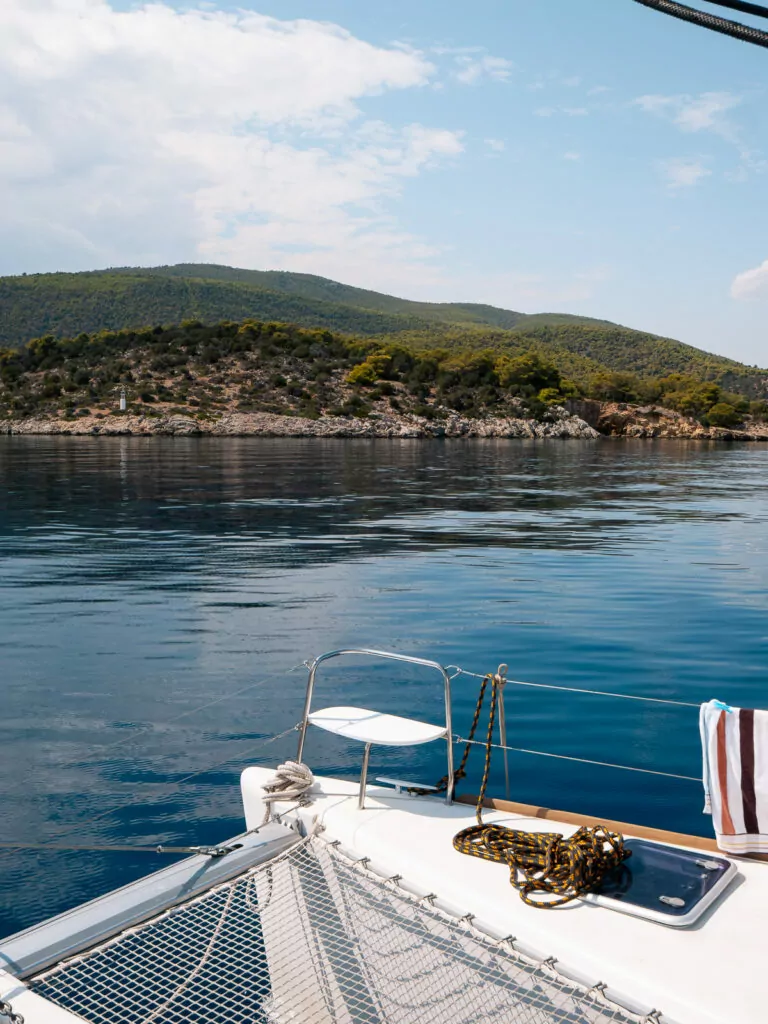 A serene view of the Aegean Sea from a sailboat deck near the Greek islands, surrounded by lush hills and calm blue waters