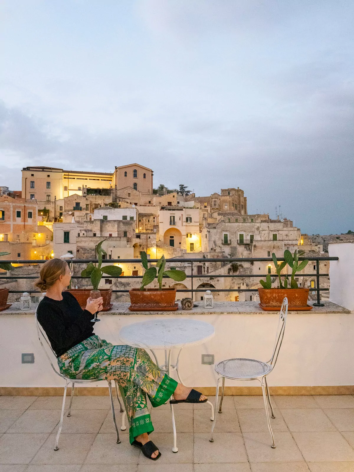 A person sitting on a rooftop terrace overlooking Matera's illuminated ancient buildings at dusk, demonstrating a perfect add on to a two weeks in Puglia itinerary.