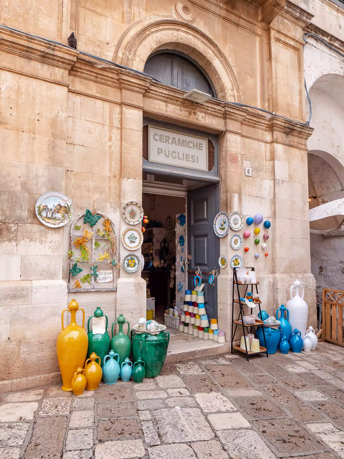 A traditional shop entrance in Puglia displaying colourful glass bottles and local products.