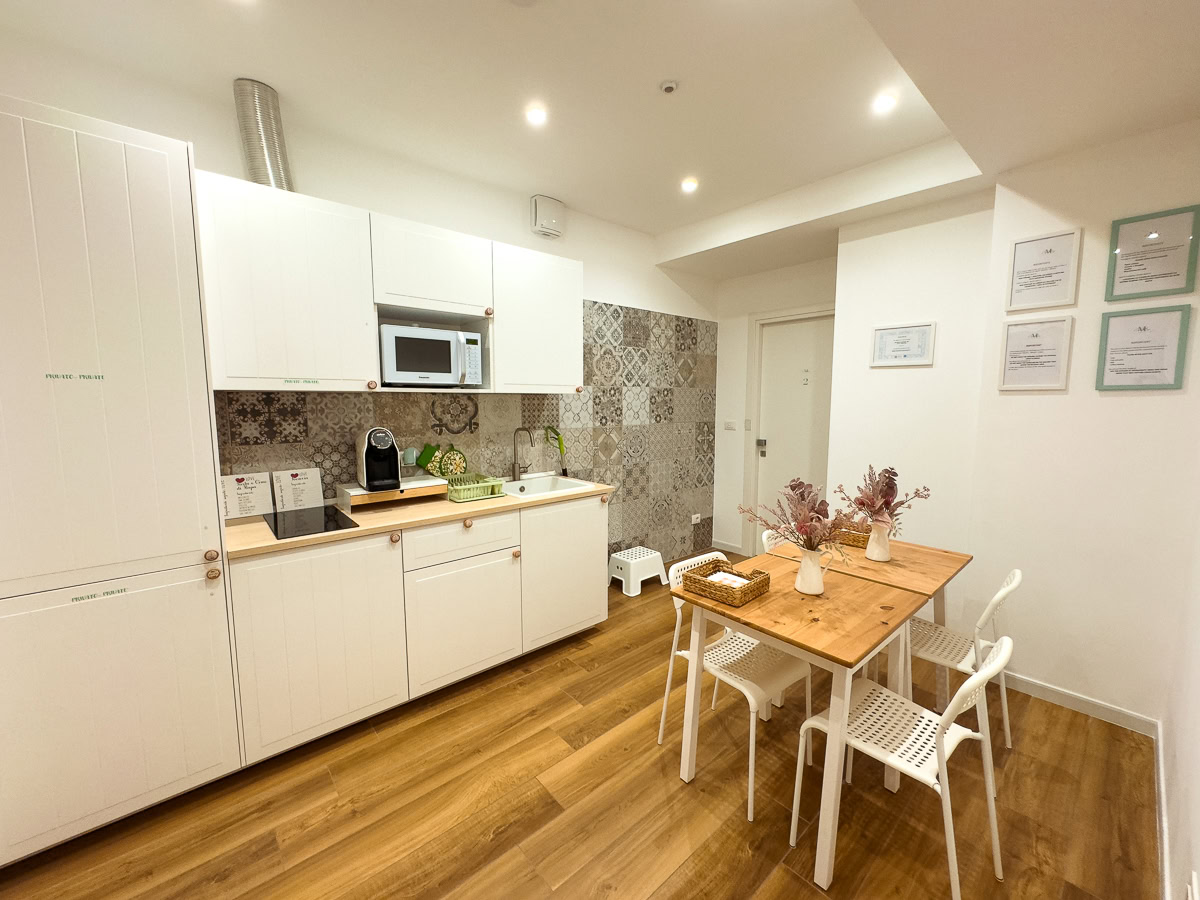 A modern apartment kitchen with white cabinets and wooden flooring, featuring a small dining area.