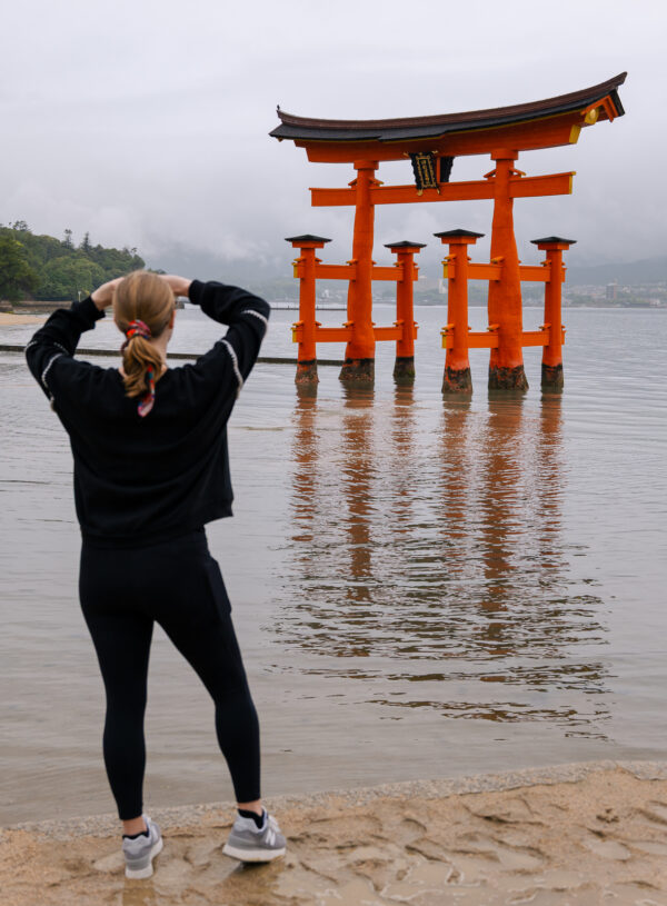 Tourist photographing iconic orange floating torii gate of Itsukushima Shrine at Miyajima Island