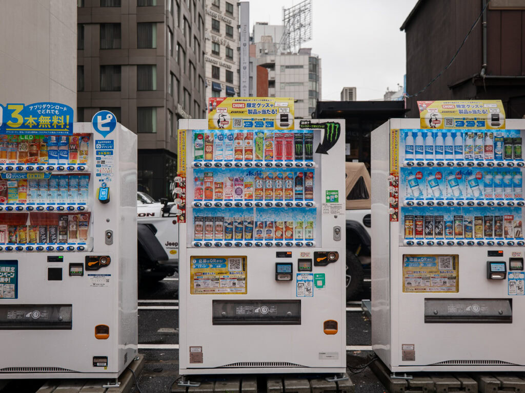 Row of colourful Japanese vending machines lined up on urban street with modern apartment buildings in background