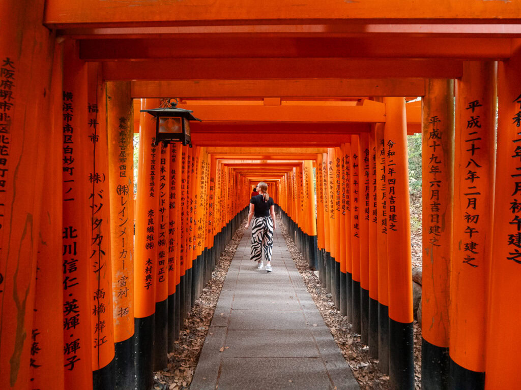 The famous Fushimi Inari shrine tunnel in Kyoto with thousands of vermillion torii gates creating a mesmerising pathway, with a lone visitor walking through