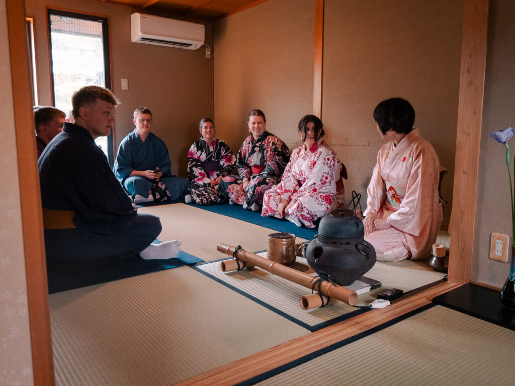 Traditional tea ceremony demonstration in Kyoto with participants in kimono seated on tatami mats around low table in authentic Japanese room