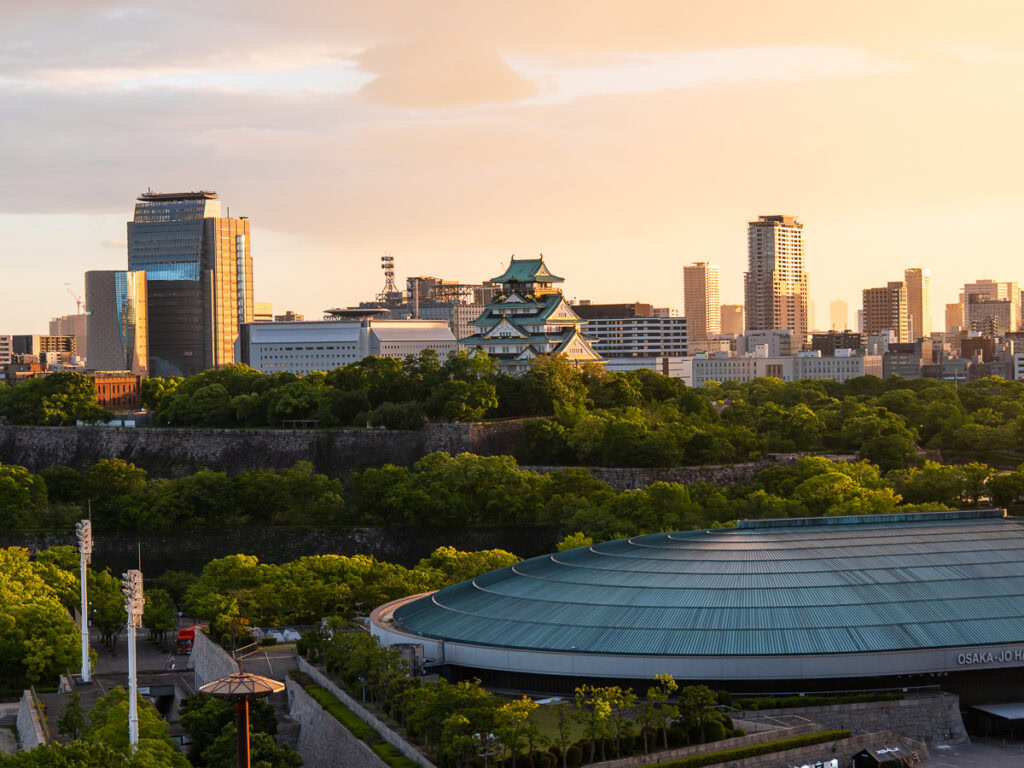 Osaka Castle and modern city skyline viewed from elevated park position during golden hour with urban towers and green spaces