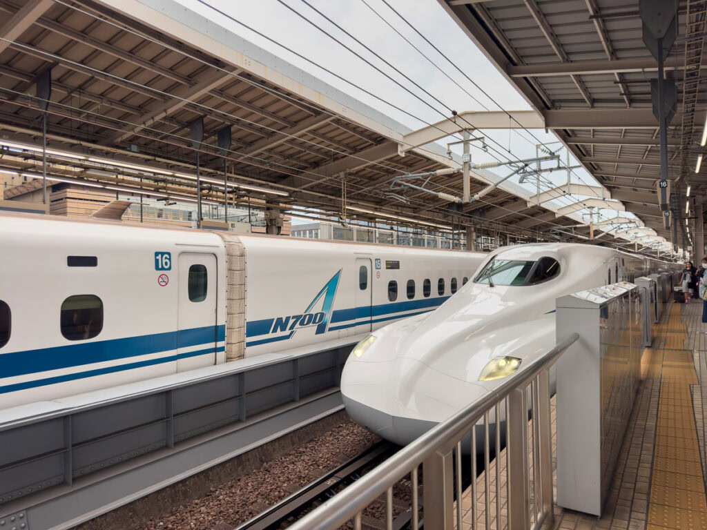White Japanese bullet train shinkansen waiting at covered railway platform station ready for high-speed journey