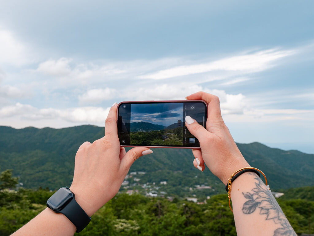a female traveller holding a phone taking photos above hakone mountain villages, using a japan esim to connect to mobile data