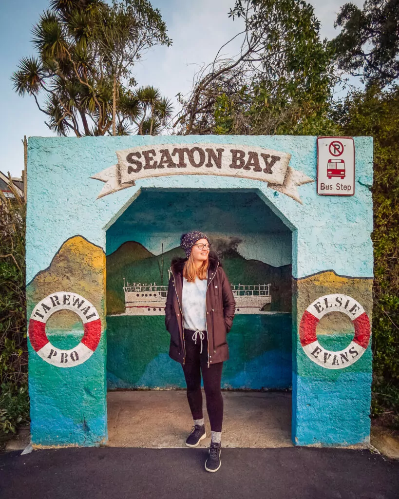 A woman standing in the painted Seaton Bay bus shelter with murals near Dunedin
