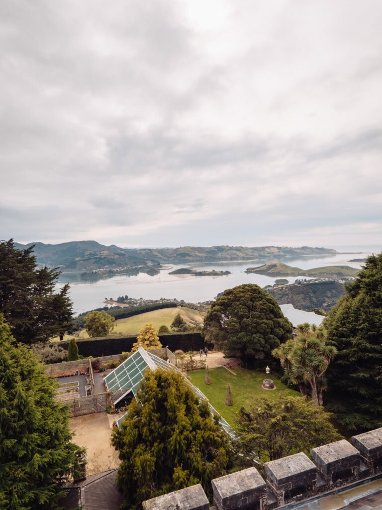An elevated view from Larnach Castle showing the formal gardens with the Otago Peninsula harbour and rolling hills in the background near Dunedin