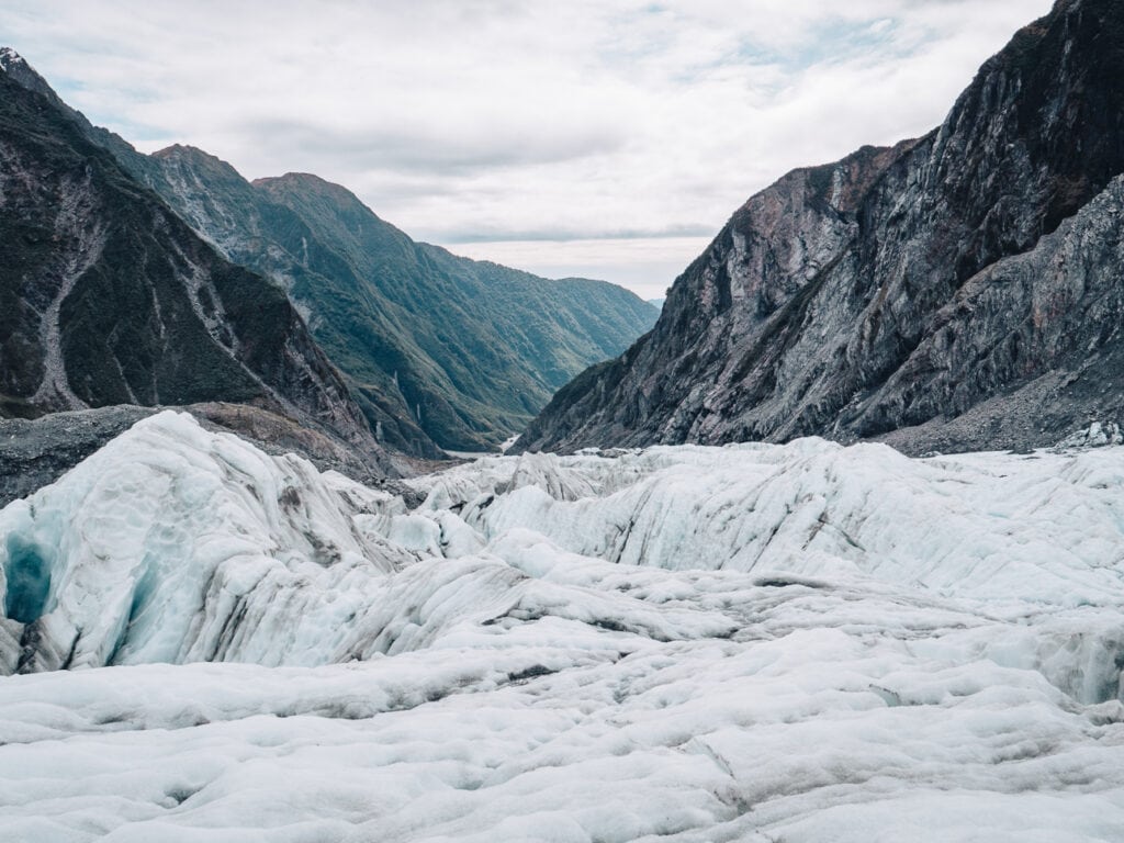 The white and blue crevassed ice of Franz Josef Glacier with steep mountain walls on either side, on the West Coast of New Zealand's South Island