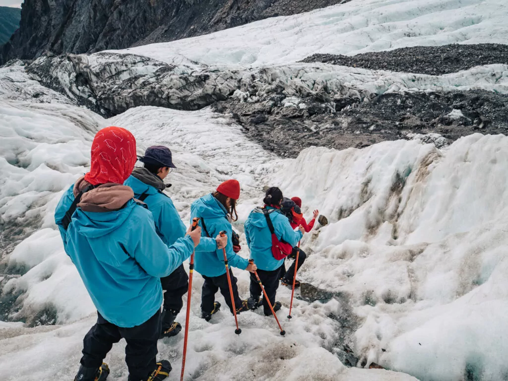 A group of hikers in blue jackets walking on the white ice of Franz Josef Glacier during a guided heli-hike tour