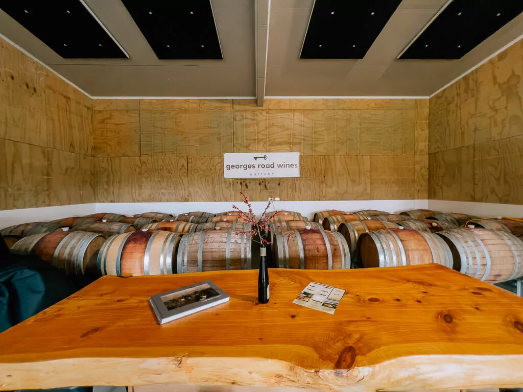 The barrel hall at Georges Road Wines in Waipara Valley, featuring rows of oak wine barrels and a wooden tasting table