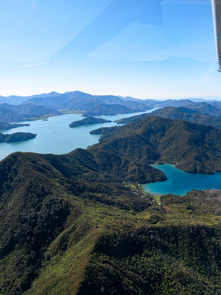 An aerial view from a small plane showing the forested hills and turquoise waterways of the Marlborough Sounds