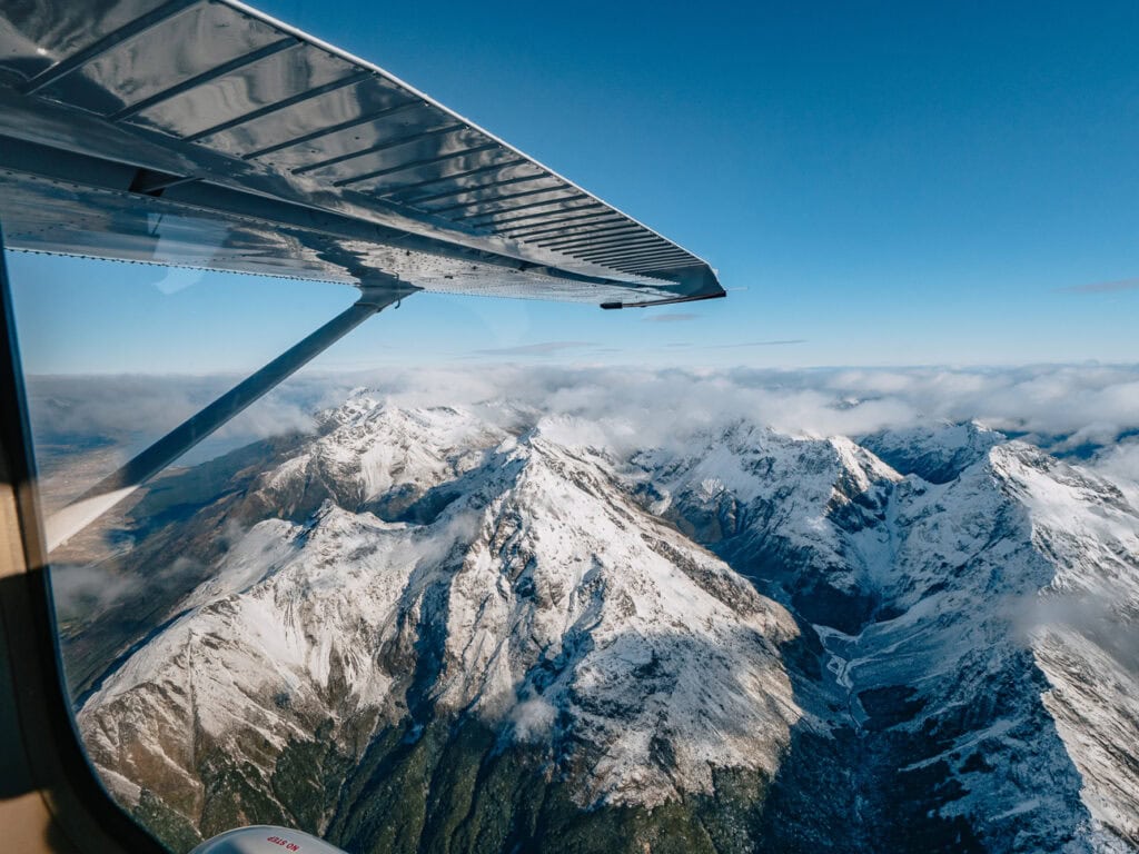 Aerial view from a small plane window showing snow-capped mountain peaks and glacial valleys in Mt Aspiring National Park
