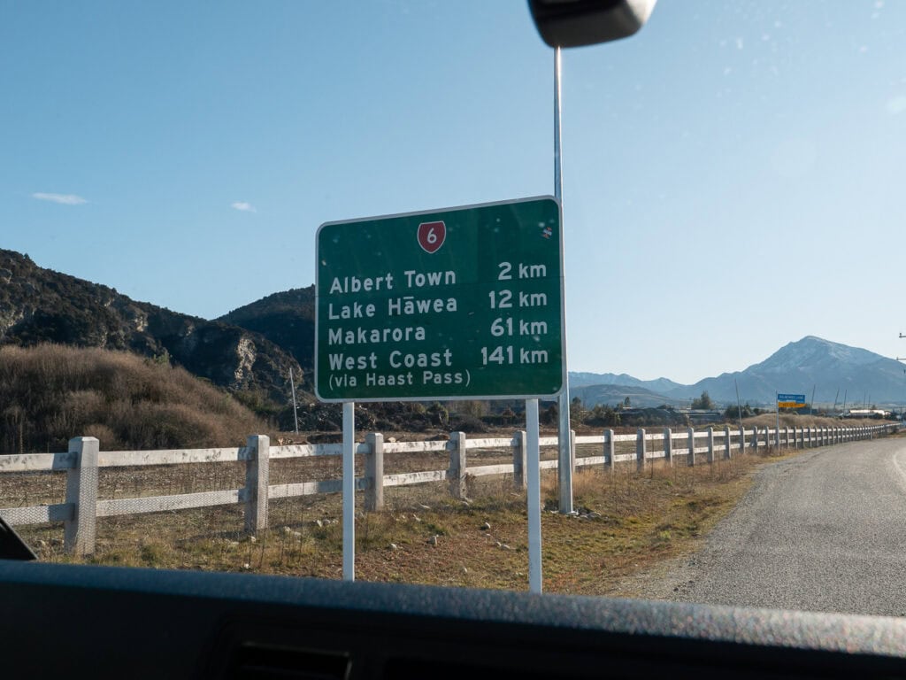 Green road sign on State Highway 6 showing distances to Albert Town, Lake Hāwea, Makarora and the West Coast via Haast Pass