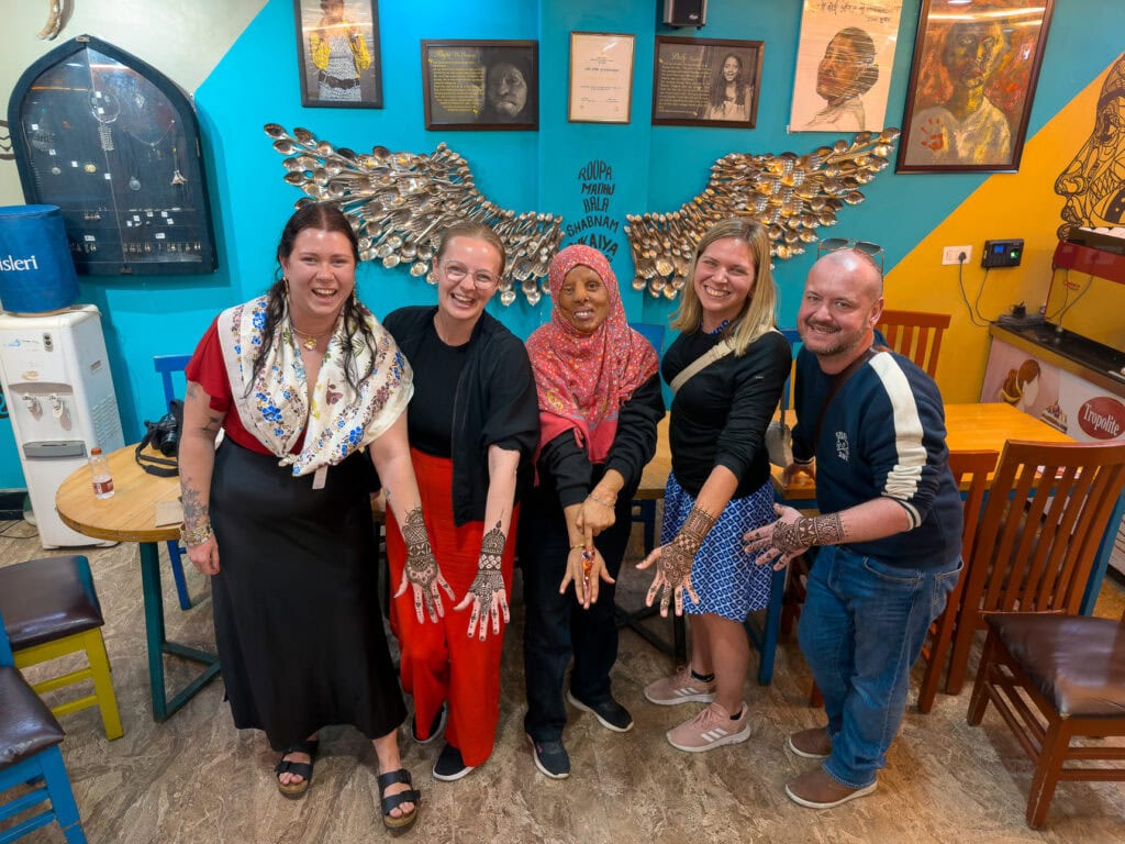 A group of travellers smile and pose together indoors against colourful walls and artwork at Sheroes Cafe in Agra. The moment reflects the social side of the One Life Adventures India experience.