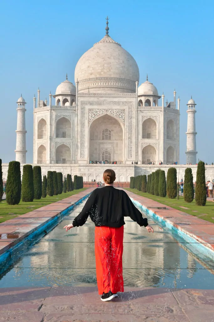 A traveller walks along the central water pathway towards the Taj Mahal with the monument perfectly framed ahead. The scene highlights a classic stop on an India tour with One Life Adventures
