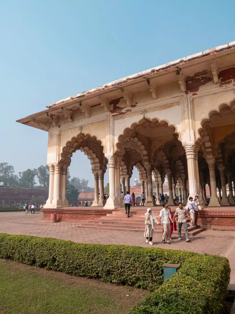 Ornate arches and columns at a historic site in Agra with detailed carvings and open walkways. Visitors walk through the shaded structure