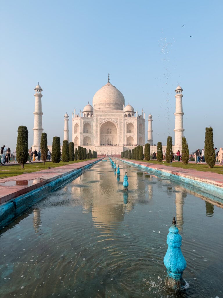The Taj Mahal reflected in its long water pool at sunrise with soft light and very few crowds. This iconic stop on an India tour shows the white marble mausoleum framed by gardens and pathways