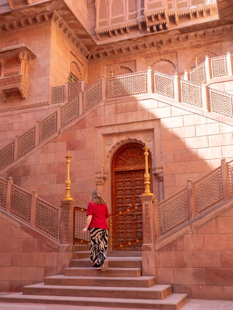 Ornate sandstone archway inside Bikaner Fort with carved details and warm orange tones. A traveller walks up the historic steps exploring the fort.