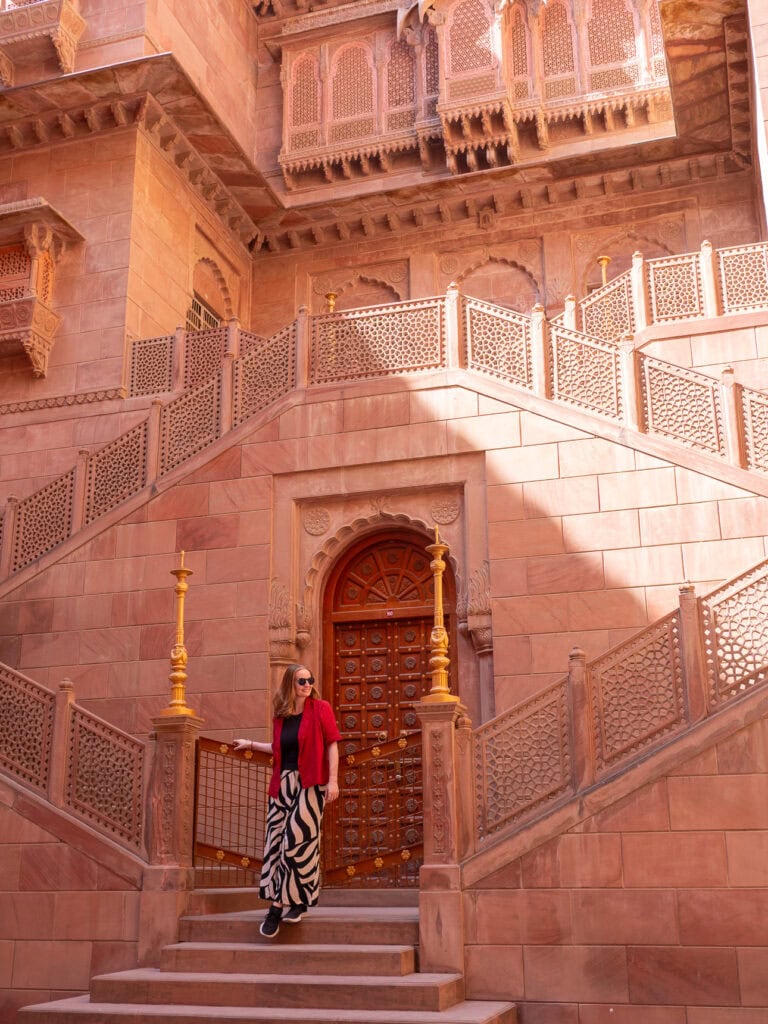 Interior courtyard of Bikaner Fort with red sandstone walls and detailed carvings. A traveller in red walks across the space surrounded by historic architecture