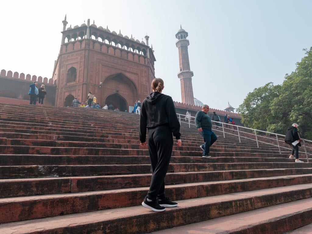A traveller walks up wide stone steps leading to Jama Masjid in Delhi with its domes and minarets towering above