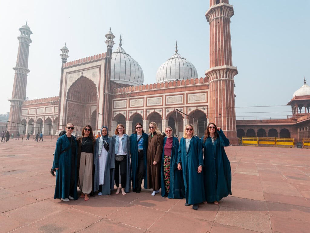 Group of travellers stand together in the large courtyard of Jama Masjid in Delhi with domes and minarets behind them on day two of the One Life Adventures India tour itinerary
