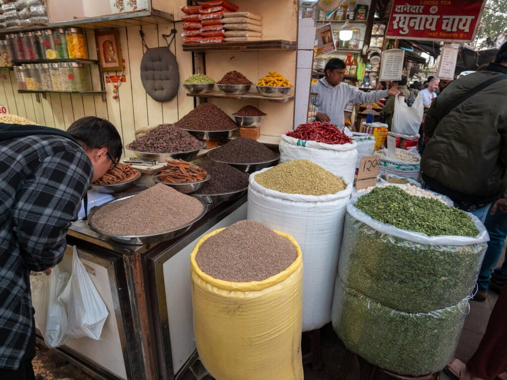 Large sacks filled with colorful spices in a busy Indian market with vendors nearby
