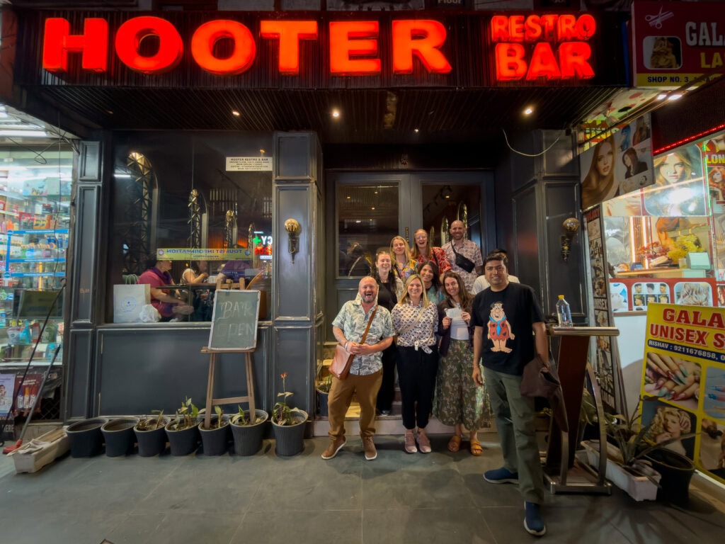 Group photo of travellers posing together outside a restaurant in Delhi at night. The group smiles after a social evening during the One Life Adventures India tour.