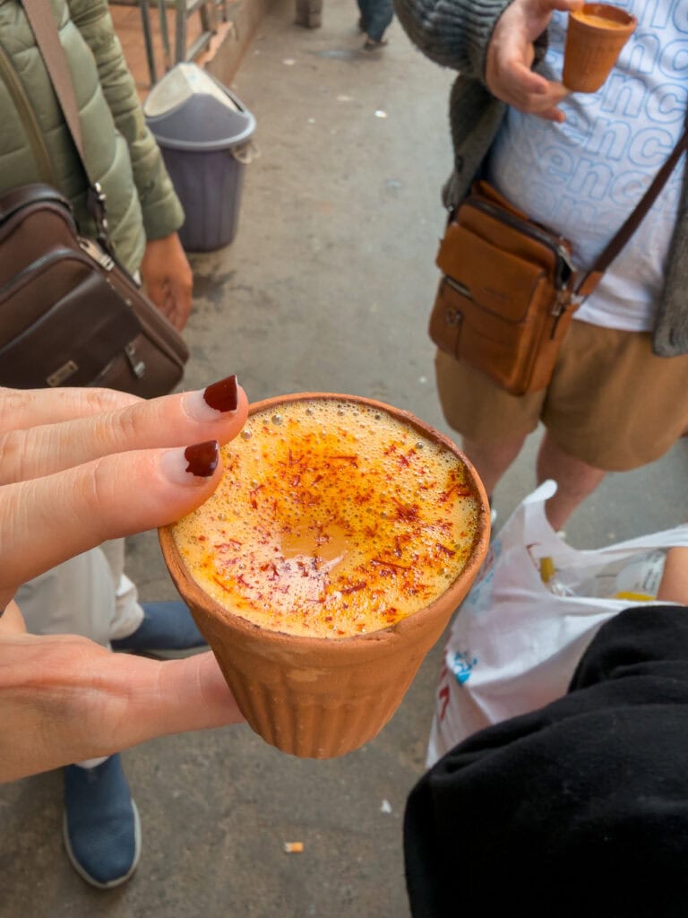 A small clay cup of masala chai topped with frothy milk and spices held in hand at a street stop
