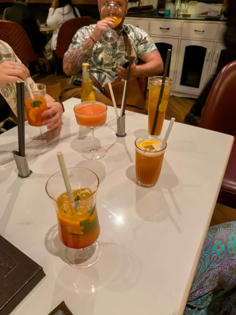 Several cocktails on a table with straws and garnishes in a lively bar setting in Delhi. Friends gather for drinks during a night out on an India tour