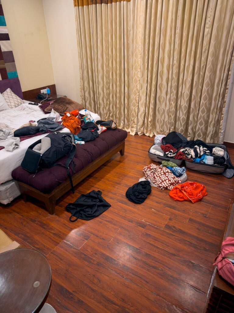 Messy hotel room with clothes, bags, and belongings spread across the floor and beds. This candid moment shows the reality of travel during a group India tour