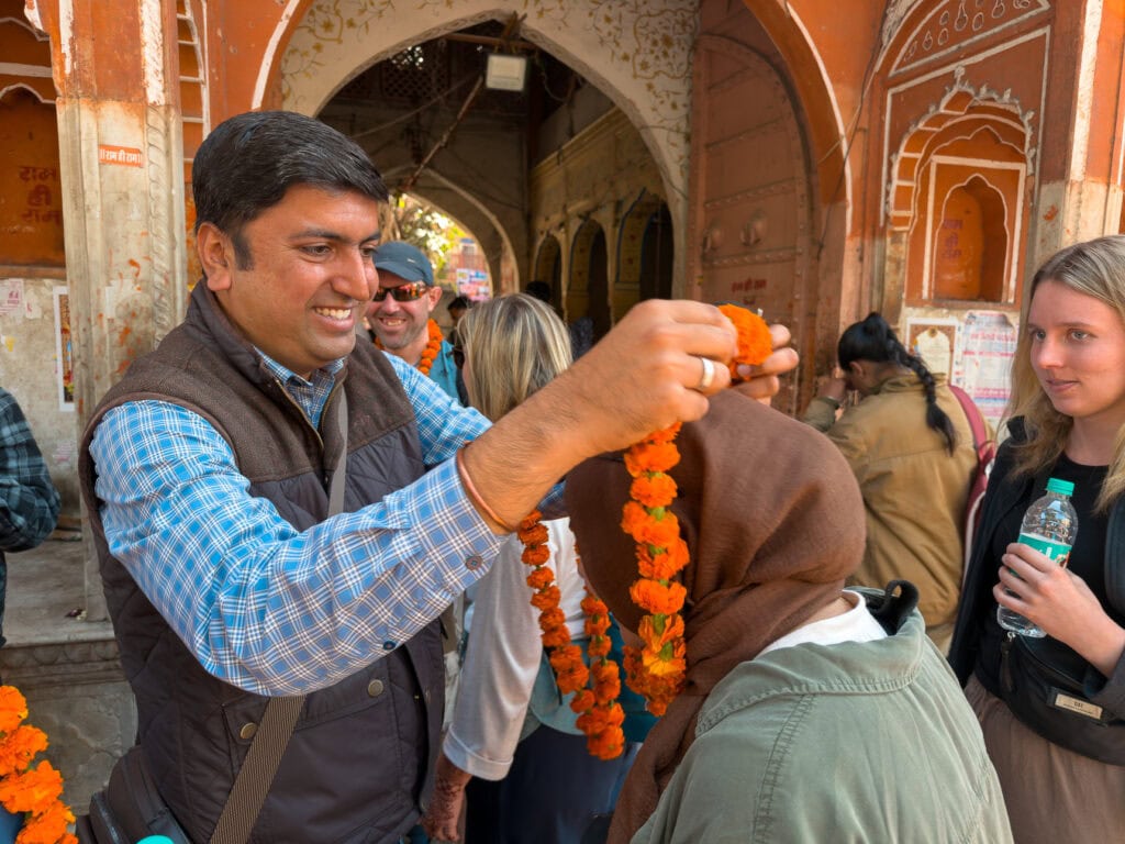 A local guide places a bright orange flower garland around a traveller’s neck in a welcoming gesture. The moment reflects traditional hospitality during an India tour with One Life Adventures