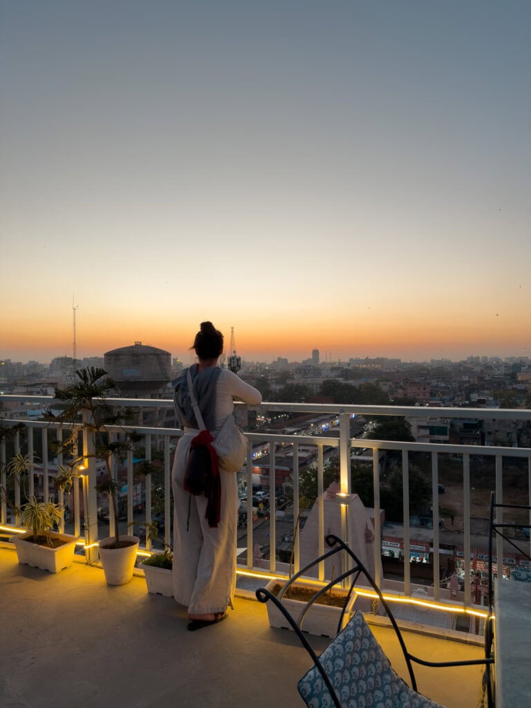 A traveller stands on a rooftop in Jaipur watching the sunset over the city with warm light across the skyline