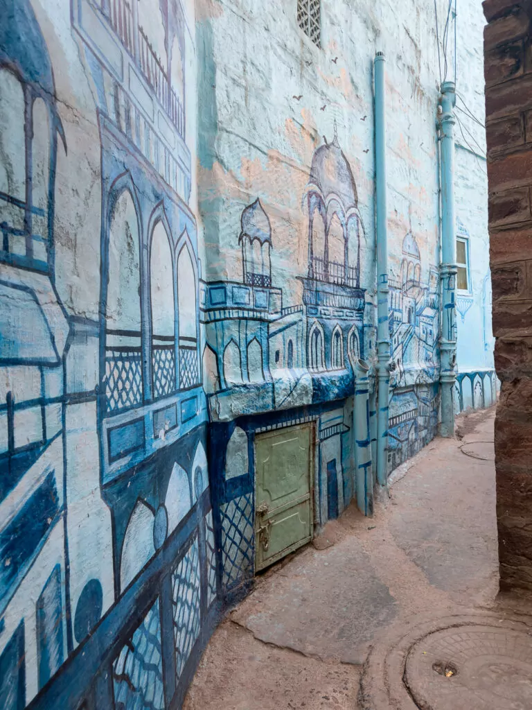 Close view of blue painted buildings in Jodhpur with textured walls and doorways and a street art mural.