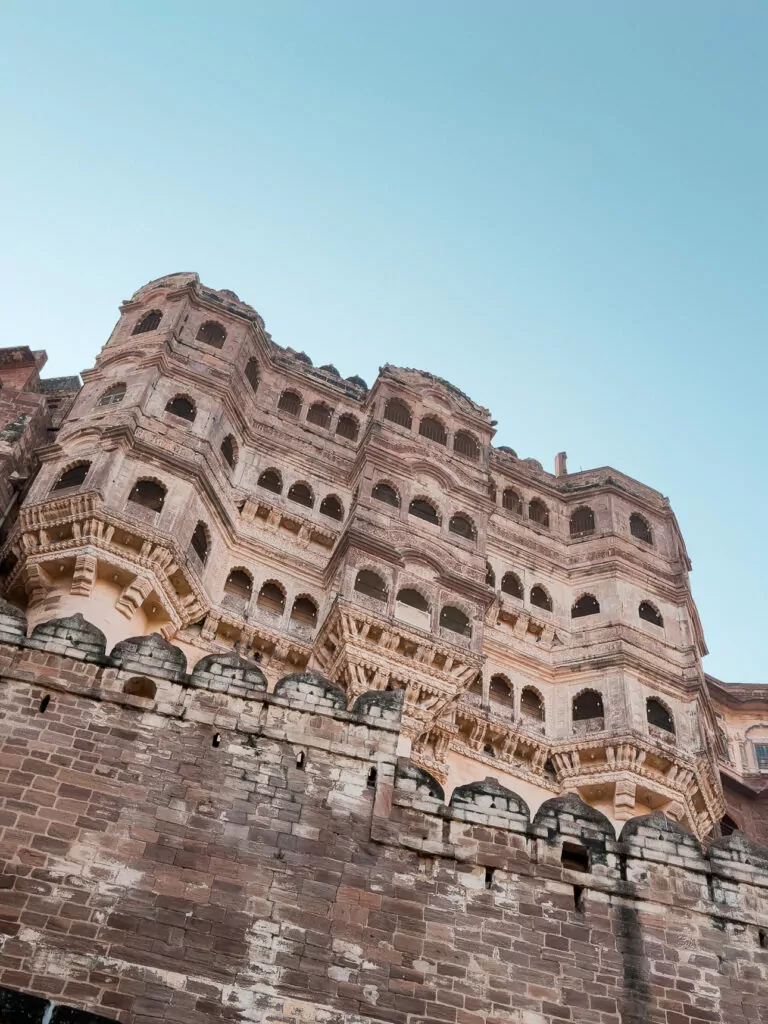 Mehrangarh Fort rises dramatically above Jodhpur with its imposing stone walls and detailed architecture. The fort overlooks the blue city below on a clear day