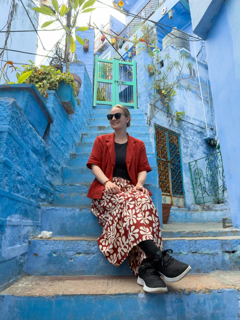 A solo traveller sits on bright blue steps in Jodhpur surrounded by painted houses and narrow streets. The vivid colours capture the charm of the Blue City during an India tour