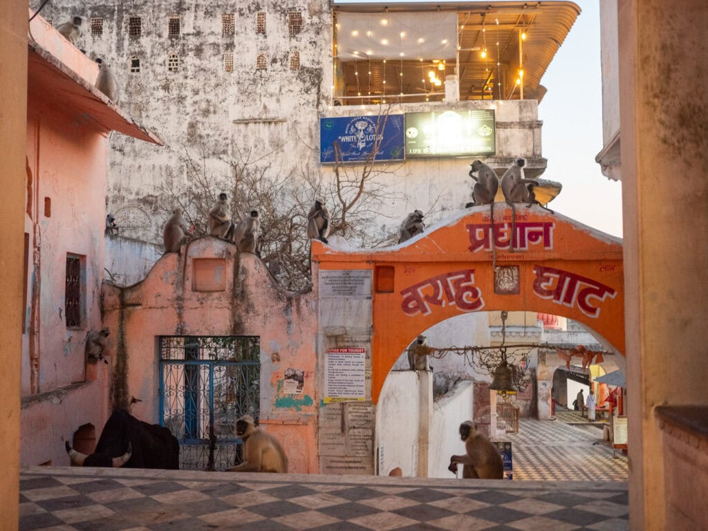 Entrance to Varah Ghat in Pushkar with an orange archway and Hindi writing above it. The worn walls and narrow passage lead down towards the lakefront