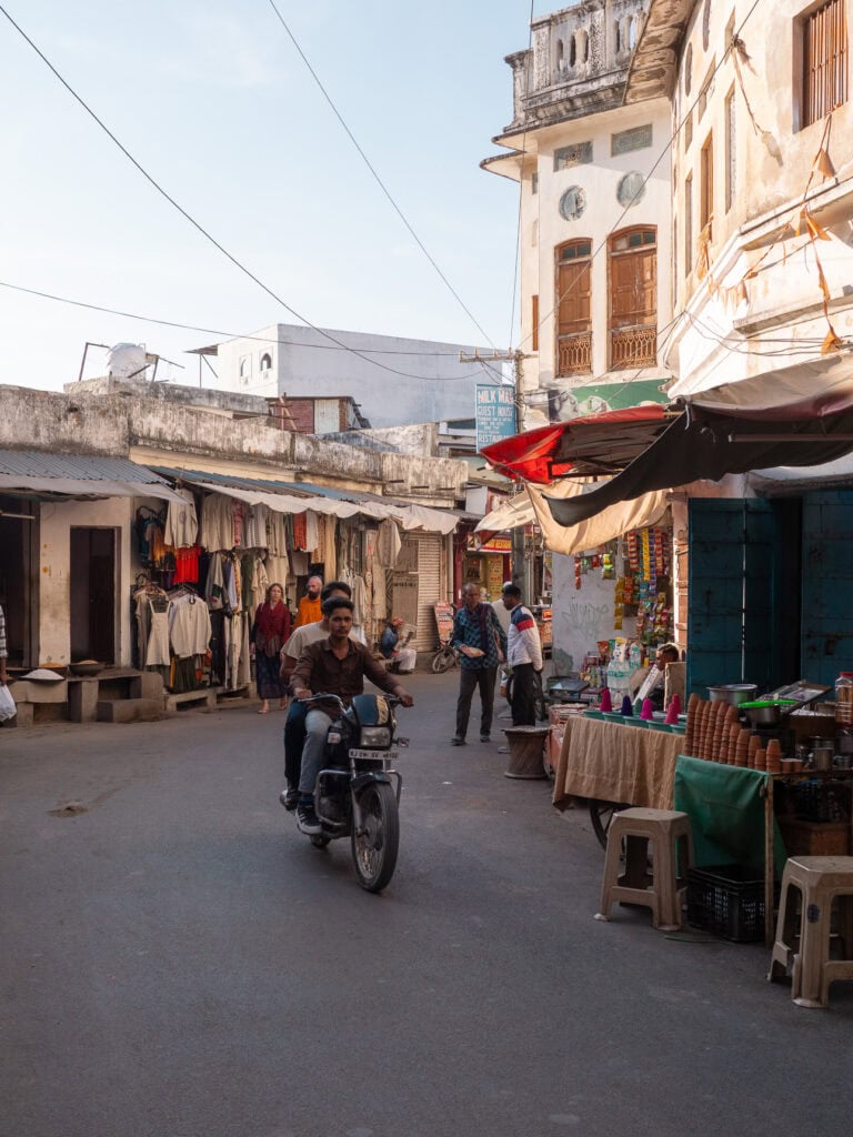 Street in Pushkar with people walking past small shops and motorbikes parked along the road