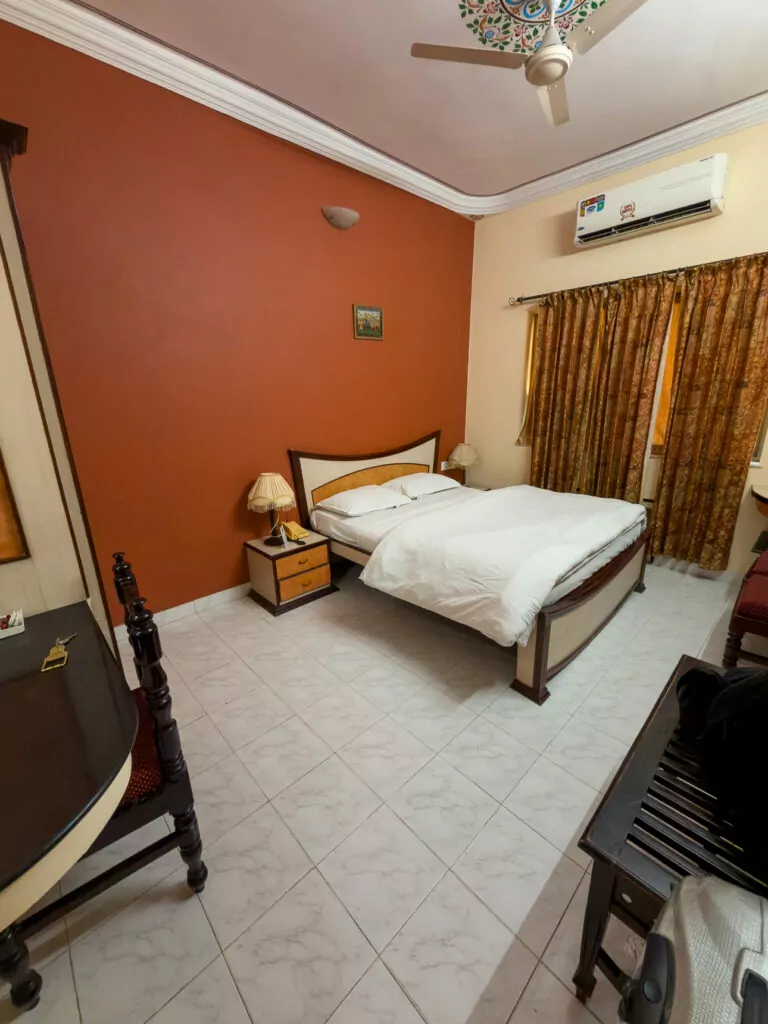 A bedroom at Pratap Bhawan hotel in Udaipur with a double bed, bedside tables, and warm coloured walls. The room includes air conditioning and simple furnishings for a comfortable stay