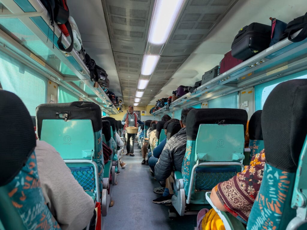 Interior of a train carriage with rows of seats and passengers travelling between Ajmer and Udaipur. The journey forms part of the One Life Adventures India Classic itinerary.