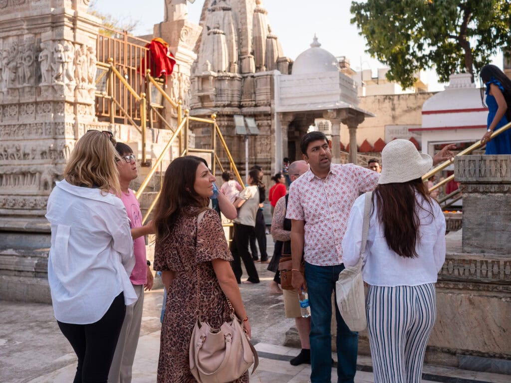 Visitors gather outside a Jain temple in Udaipur with detailed white stone architecture and sculpted towers. The scene shows a cultural stop during an India tour