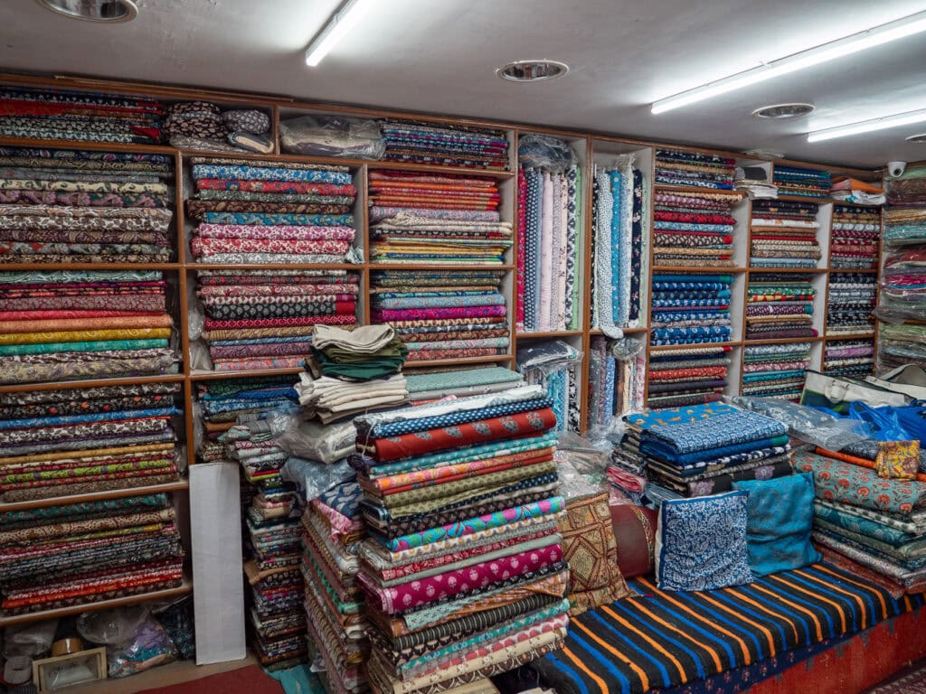 Interior of a textile shop in Udaipur filled with neatly stacked colourful fabrics and patterns. Shelves are lined with folded materials from floor to ceiling