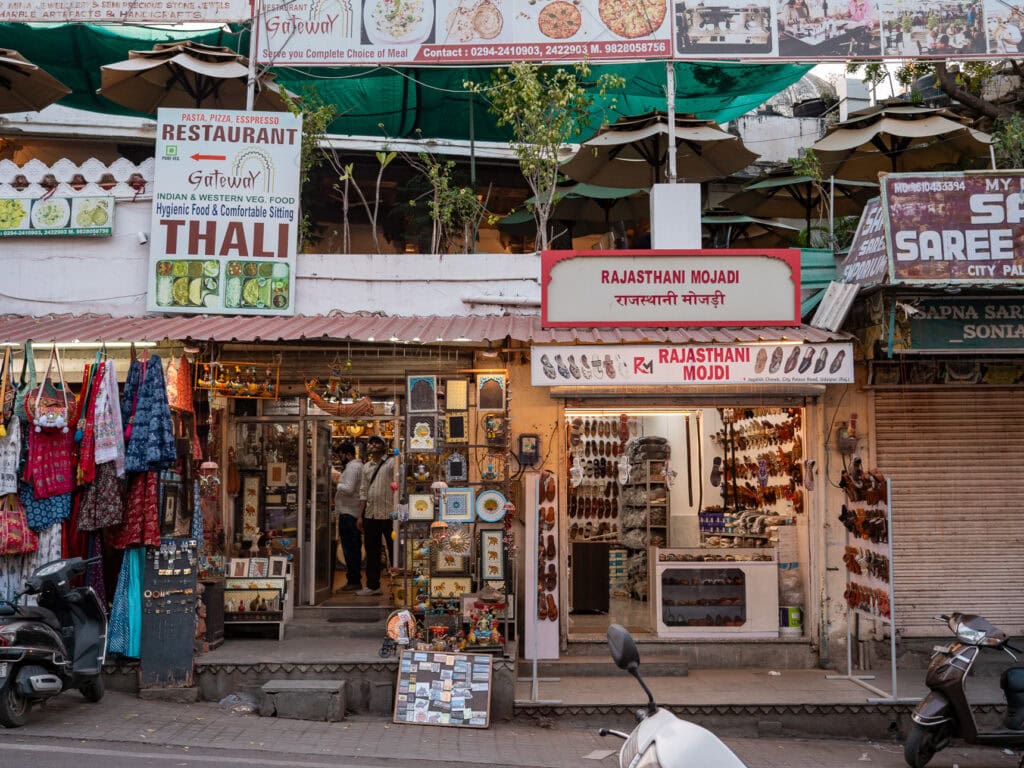 Street scene in Udaipur with shops, signs, and people walking past local businesses