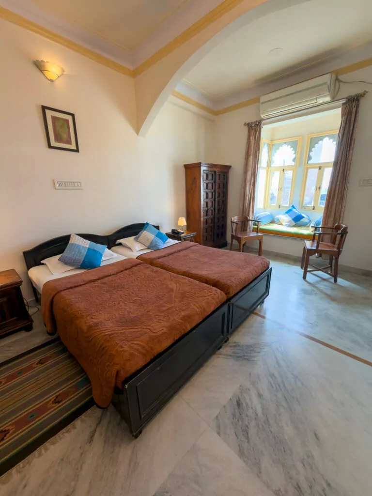 Bright bedroom at Pratap Bhawan in Udaipur with a large bed, natural light from the window, and classic furnishings