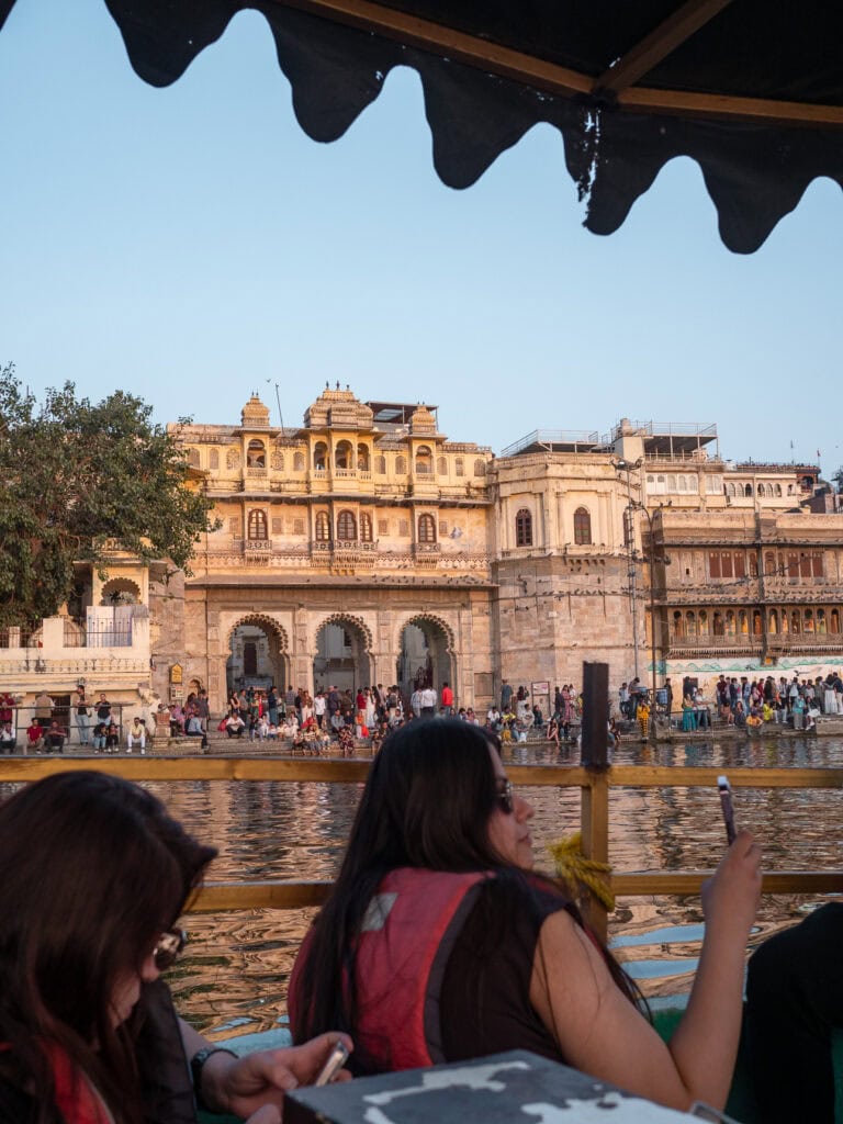 Boat cruise on Lake Pichola with views of palaces and buildings along the water. The calm lake reflects the soft evening light in Udaipur