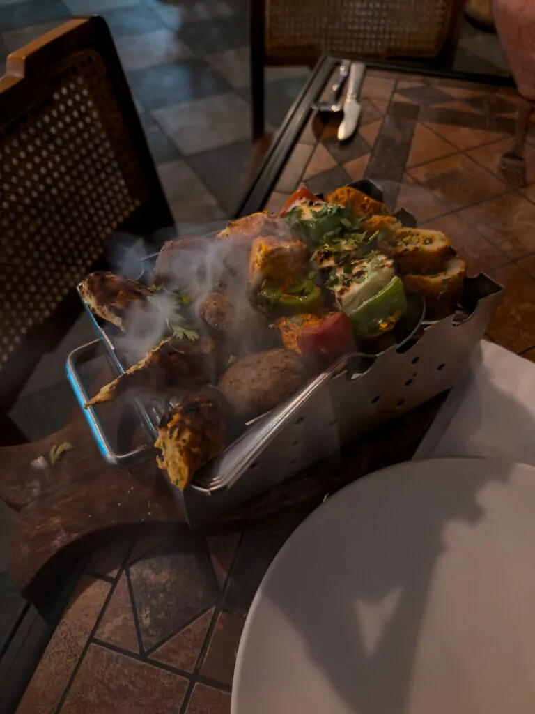 A sizzling tandoori dish served on a hot plate with smoke rising and vibrant garnishes. The meal showcases local flavours during an India tour