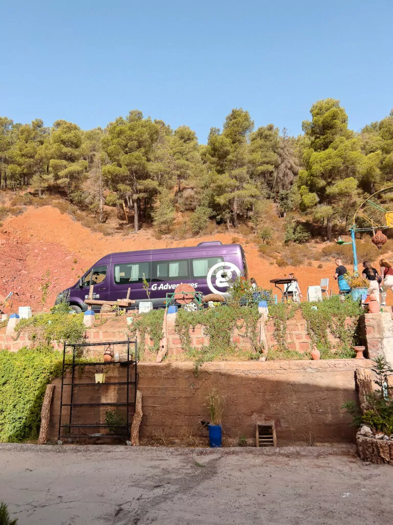 G Adventures tour bus parked at a stop in Morocco surrounded by greenery and red earth