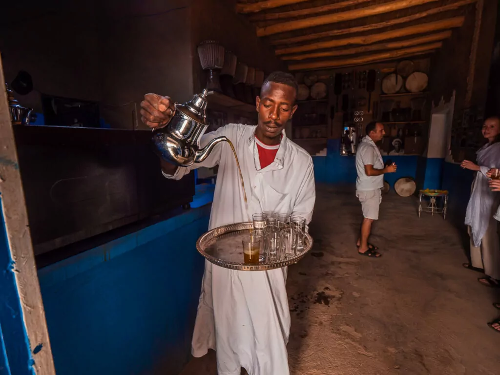 Berber man in traditional white clothing pouring tea at a nomadic camp in Morocco