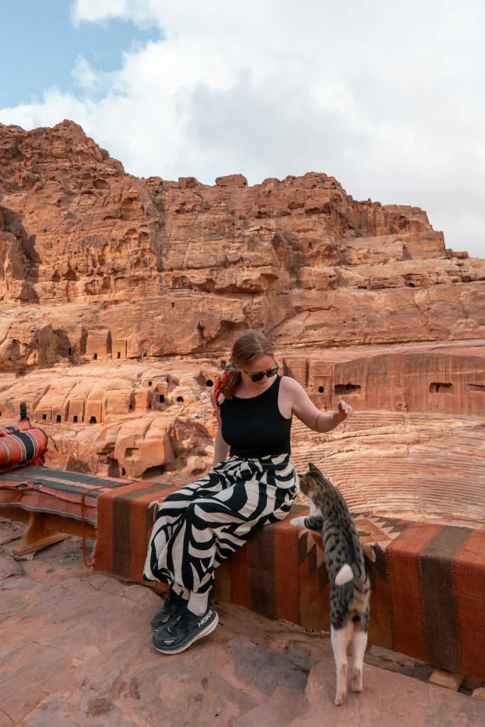 Woman sitting on a stone ledge at Petra with red sandstone rock formations in the background